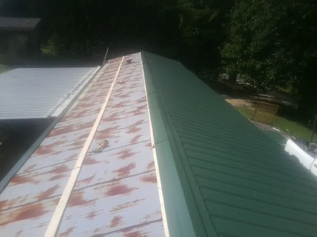 Old rusted panels beside newly installed green metal roofing — Wind Damage Roof Repair by Roofing Brothers in Victor